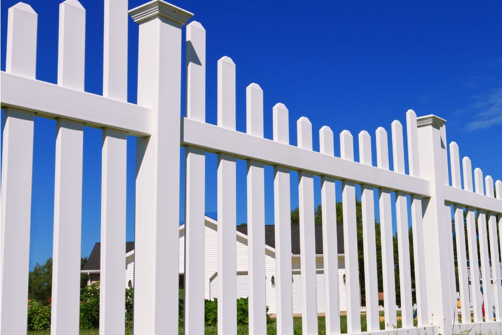 A white vinyl picket fence running along a property line under a clear blue sky